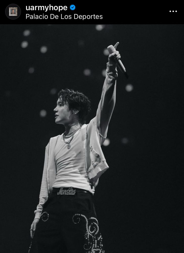 A black and white photo of an Asian man on stage [J-Hope of BTS], wearing a hoodie with white tank top. He was holding his mic with his left hand.