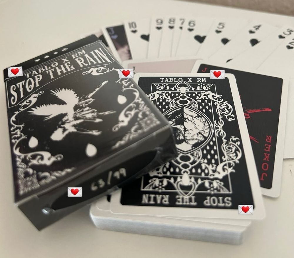 A playing card deck on a white surface. The back of the cards says “Stop The Rain” and “Tablo X RM”
