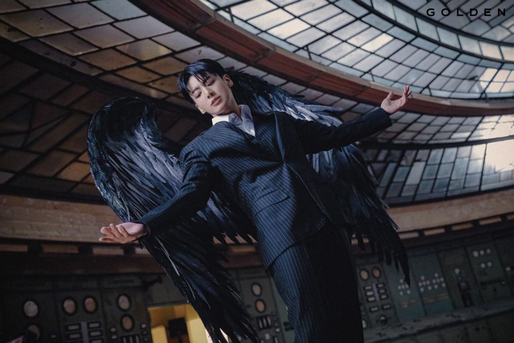 An Asian man [Jungkook of BTS] wore blacksuit jacket and feathery wings