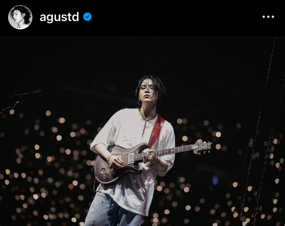 An Asian man [SUGA of BTS] played guitar on stage. He was closing his eyes.