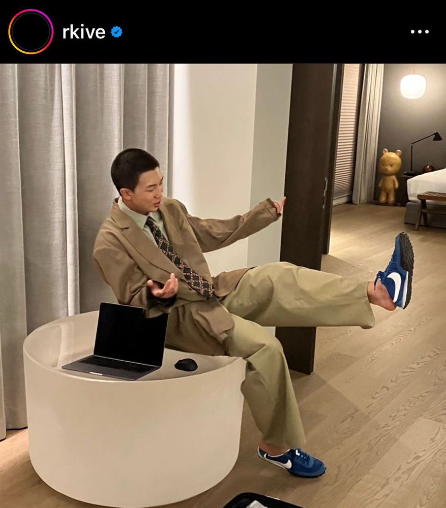 An Asian man [RMnof BTS] sitting on an artwork by Roni Horn at his home.
He was wearing khaki/olive suit & pants, and blue sneakers.
On Roni was also a laptop & a mouse