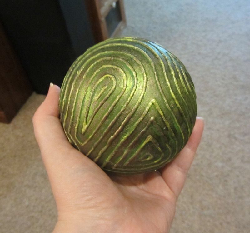 Photo if an olive green orb, about 4-5 inches in diameter. A raised "finger print" pattern is painted onto the surface using puff paint