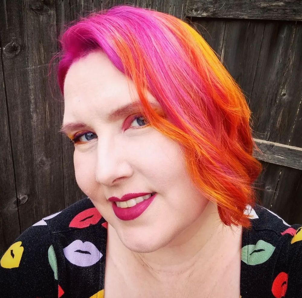 A selfie photo of Amy Avery - a white woman with pink and orange and red hair, and pink lipstick
