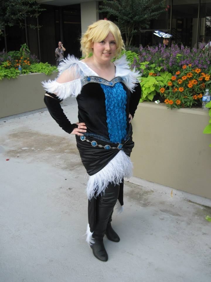 Amy as Maevaris Tilanu from Dragon Age, in cosplay. A woman with short blonde hair and a black dress with blue and silver trim.