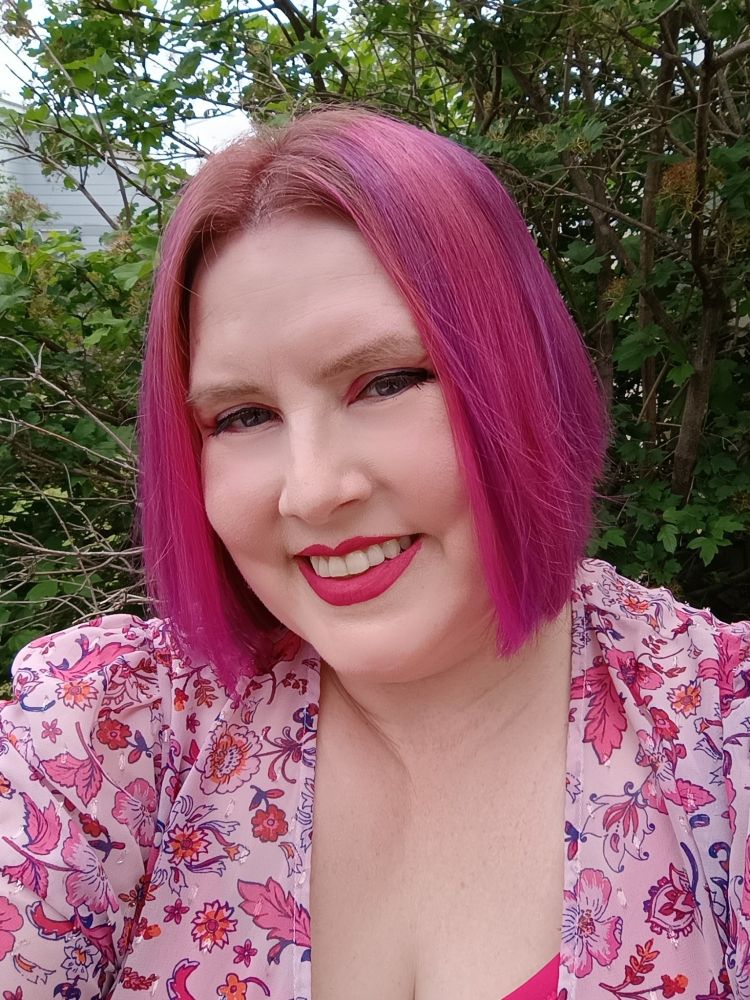 Photo of Amy, a white woman with a pink bob wearing a pink floral top