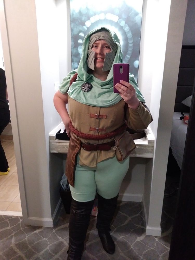 Amy as Scout Jim from Dragon Age Inquisition, in cosplay. A tan vest with mint green hood and leggings, and a gray helmet.