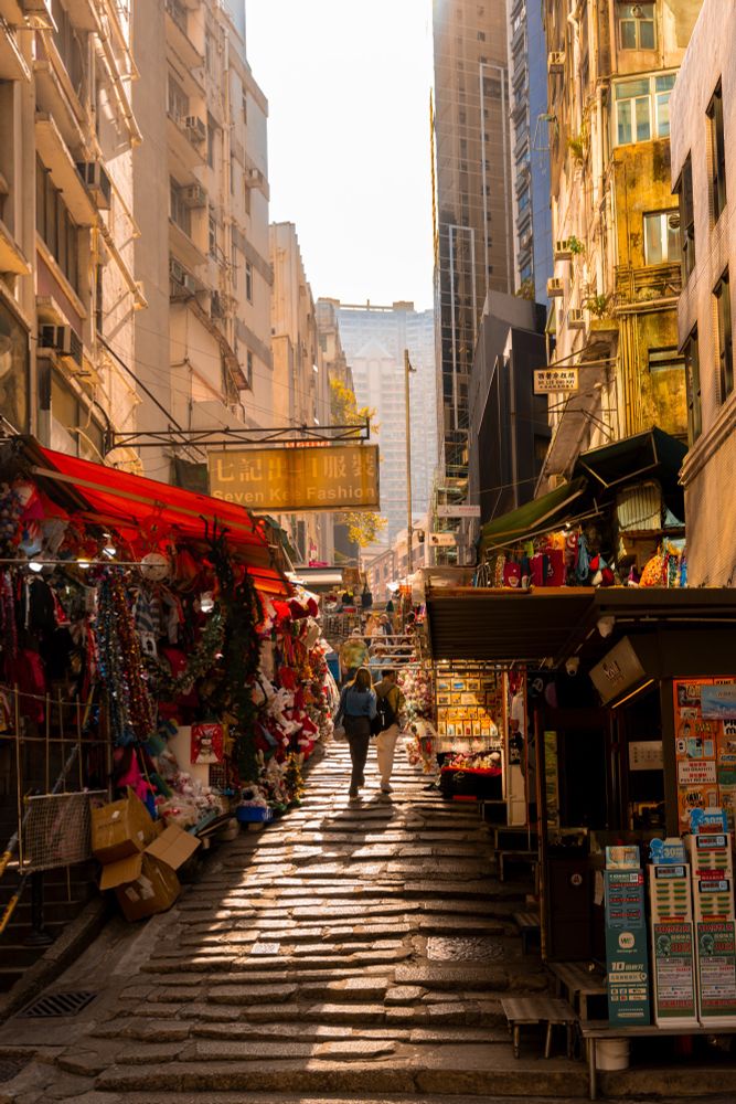 A couple walks up a stone staircase flanked by tall buildings in Hong Kong