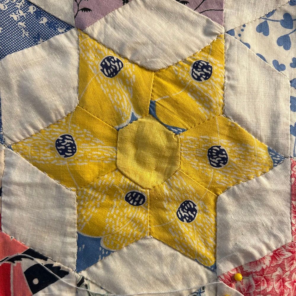 A six-pointed quilted star made of fabric with a stylized yellow poppy print with a blue background peeking through and a solid yellow hexagon at the center of the star