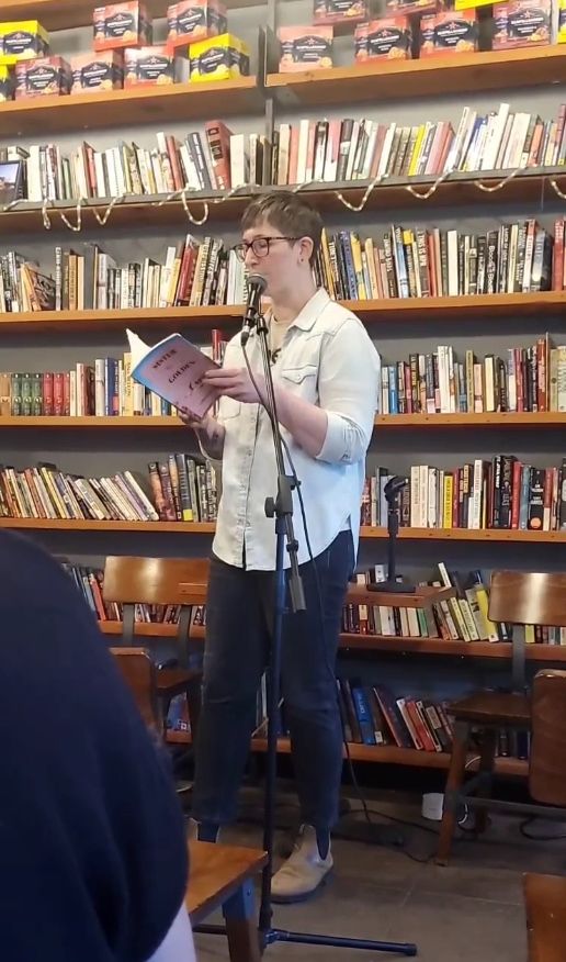 Me reading in front of a wall of books at The Stacks Coffeehouse