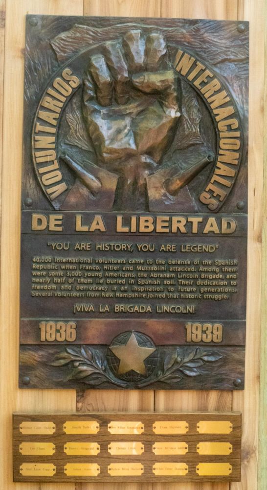 A bronze plaque featuring a large fist in the center and the words, “Voluntarios Internacionales de Libertad,” Spanish for International Volunteers for Freedom.  In smaller letters, the plaque reads, “You are history, You are legend.  40,000 international volunteers came to the defense of the Spanish Republic when Franco, Hitler, and Mussolini attacked.  Among them were 3000 young Americans, the Abraham Lincoln Brigade, and nearly half of them lie buried in Spanish soil.  Their dedication to freedom and democracy is an inspiration to future generations.  Several volunteers from New Hampshire joined that historic struggle.” 

“¡Viva la Brigada Lincoln!” it says underneath.  