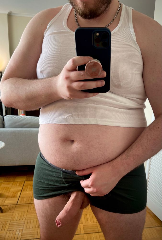 A beefy gay bear pulls his shorts up to reveal his fat cock and balls. His fat belly spills out of his undershirt and overhangs his waistband