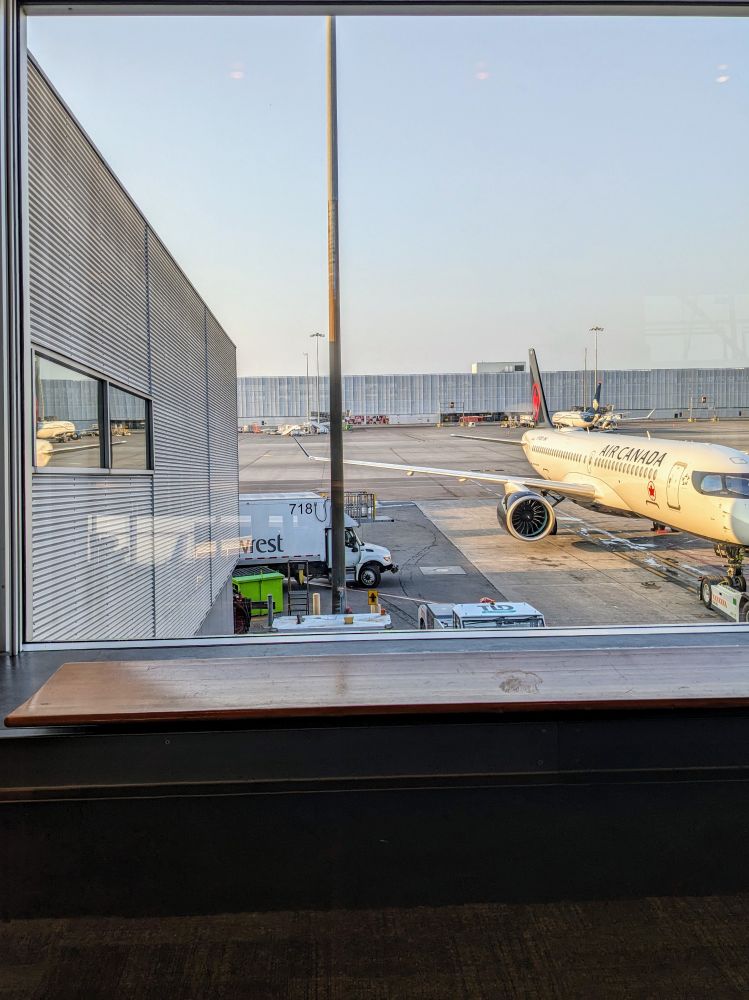 A picture from an airport window. We can see a plane to the right. A truck is approaching it from the left.