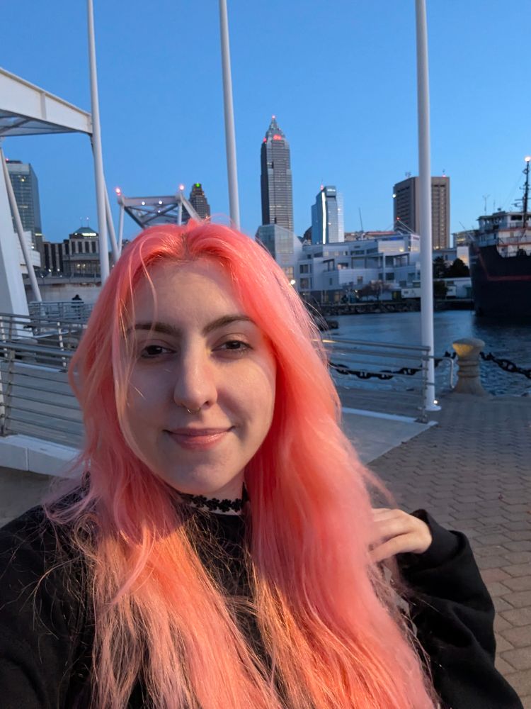 selfie of Allison with wind-tousled at twilight with Cleveland and a small drawbridge in the background. it's a haphazardly positioned photo, don't worry about the terrible composition please