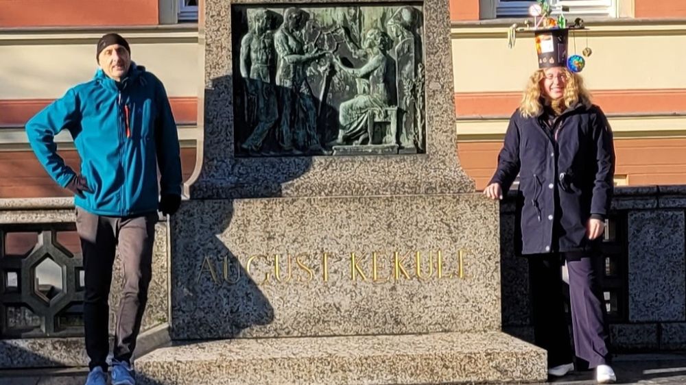 Julia and her PI Stefan Grimme stand on either side of a statue of August Kekulé. Julia wears a traditional handcrafted PhD hat.