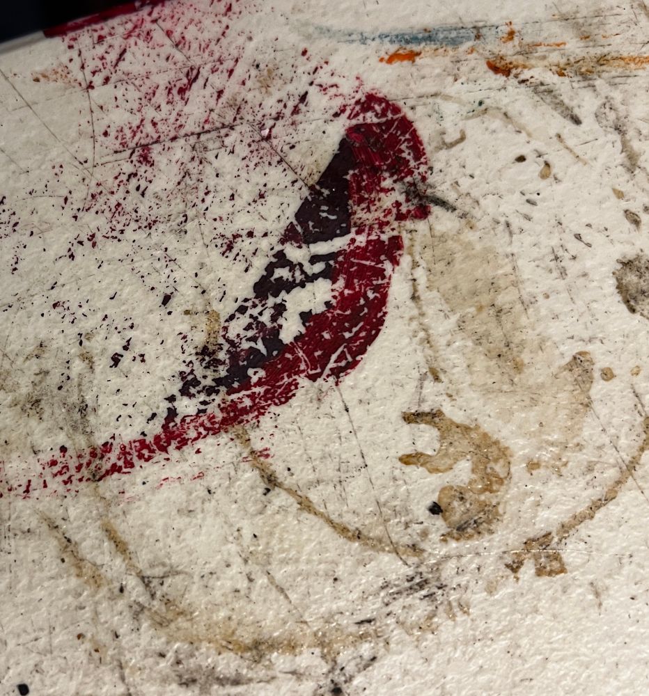 A picture of a mixture of stains on a white plastic table. A coffee ring becomes a branch where a two-toned pink bird made of spilled paint perches for a little rest. 
