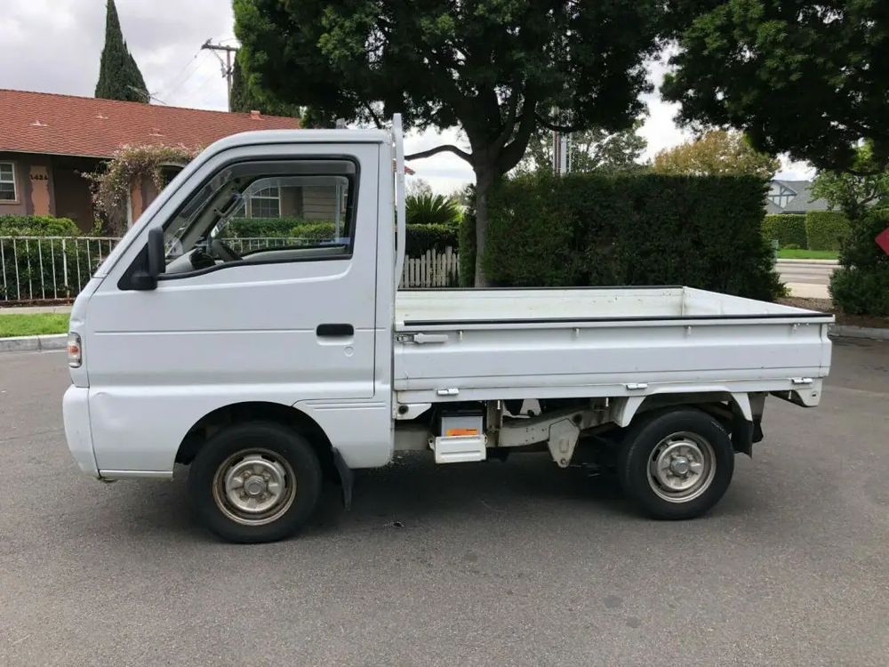 Parked white Kei truck in suburban setting, left side profile.