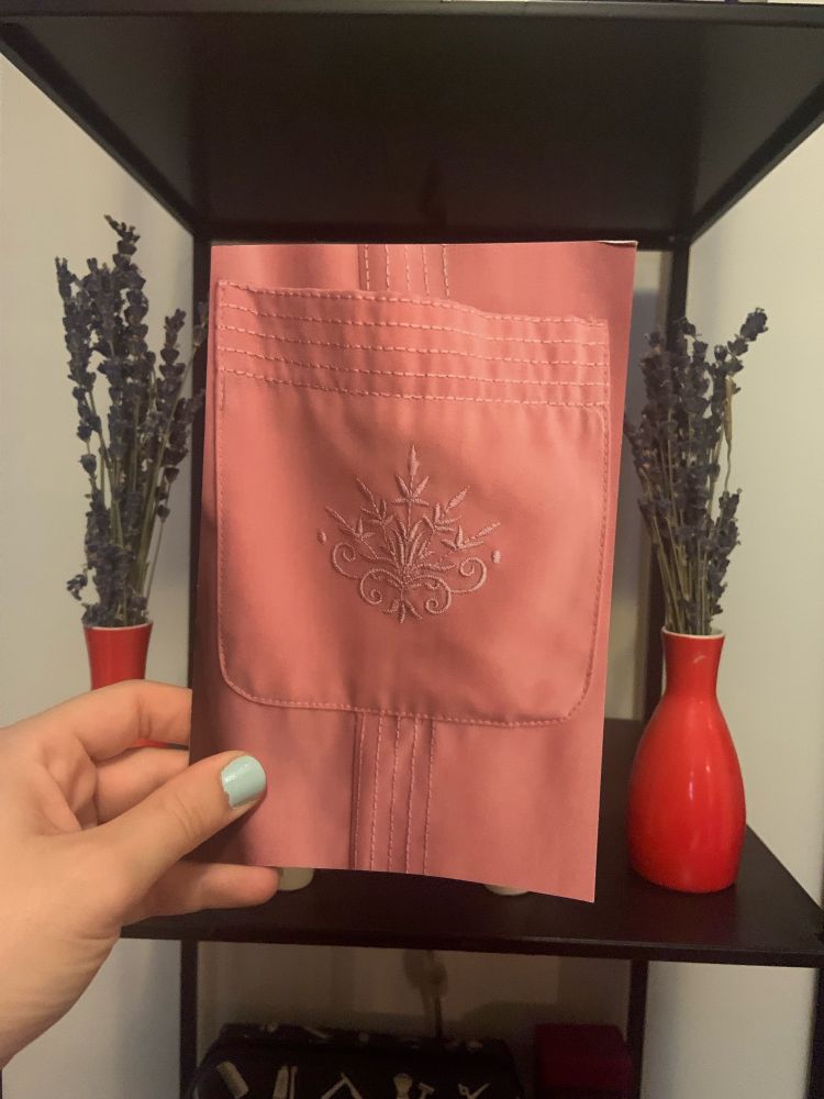 Chapbook held between two vases containing dried lavender. Cover features a pink pocket with embroidery.