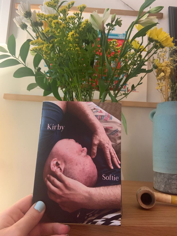 The chapbook held in front of a vase of flowers. Cover showing Kirby (beautiful, in repose).