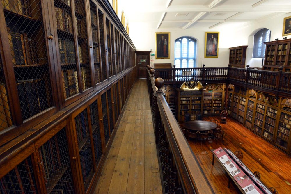 Photo of an old library with wooden shelving and a balcony.