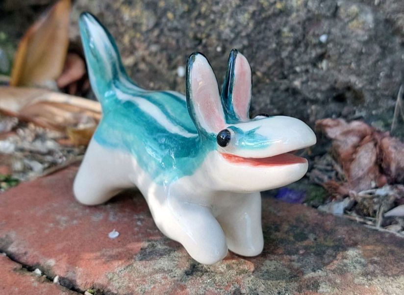 the same ceramic animal from another angle. its front foot is raised, as if in motion. teal and white stripes run along its body like a skink.
