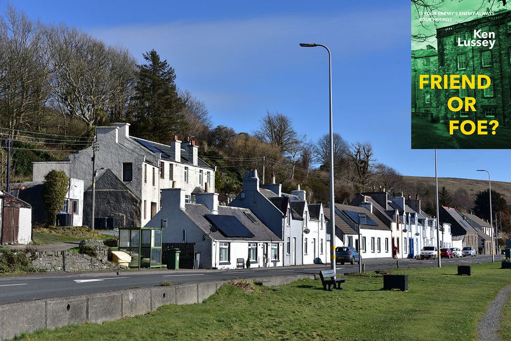 This modern image shows part of Cairnryan in Galloway. A road crosses the frame from the bottom left corner to the lower right. On its near side is a grassy area that fills the bottom right of the frame. On the far side of the road is a line of houses and cottages mainly finished in white, with some houses on a higher level at the near end. Behind the buildings is a wooded hillside. The sky is blue. The front cover of ‘Friend or Foe?’ is shown in the top right corner.