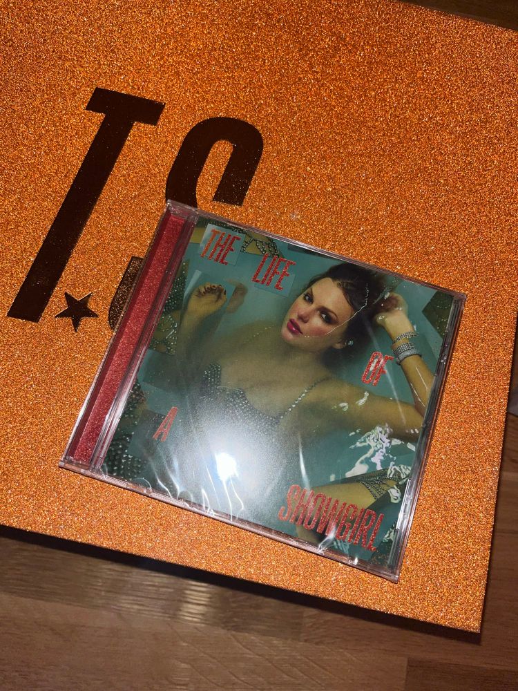 a the life of a showgirl cd is laying on top of a sparkly orange box with the letters t.s on it
