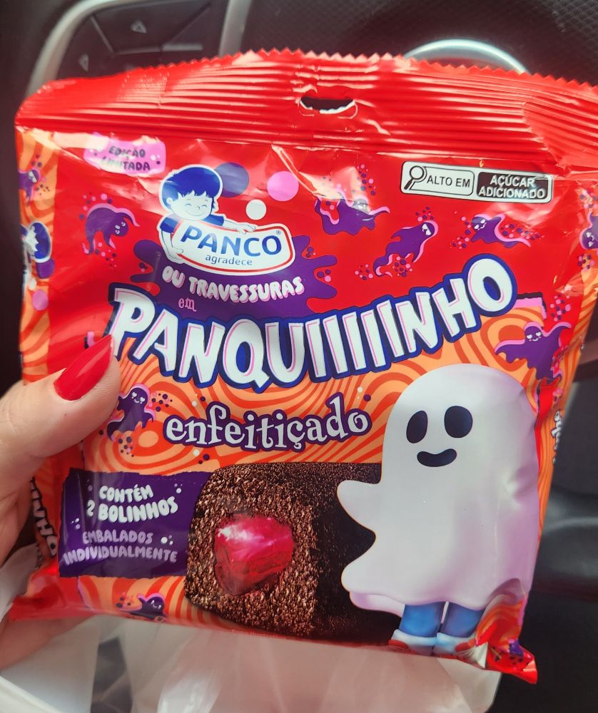 Mão segurando pacote de bolinho Panco com tema do halloween. A embalagem diz "panquiiiiiinho enfeitiçado" e há a figura de um menino com lençol por cima, simulando um fantasma. 