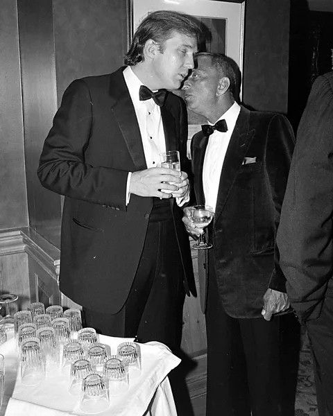 Roy Cohn whispering to a young Trump (both look inebriated).