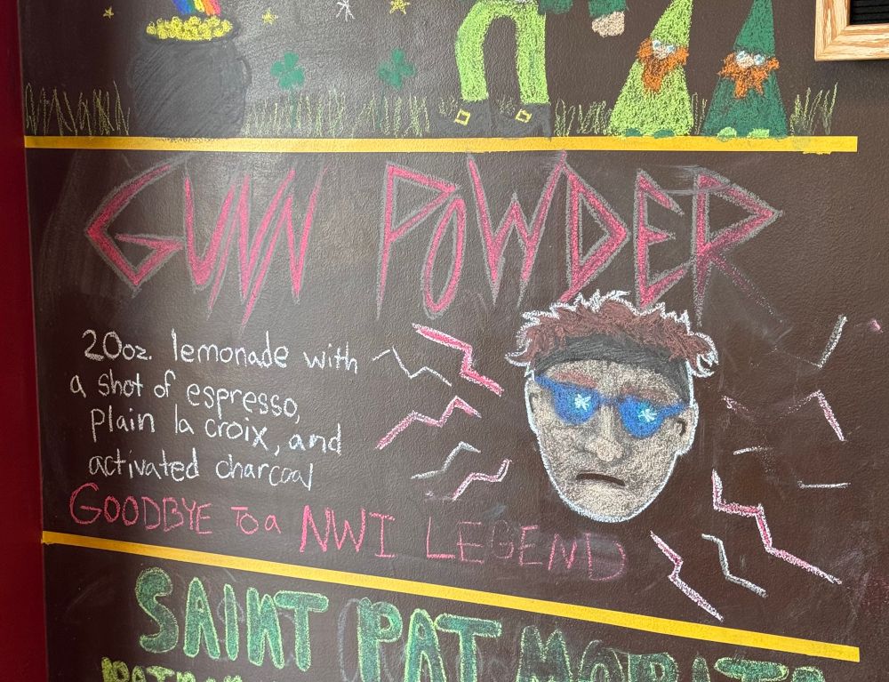 A chalk menu at a cafe offering “Gunn powder” which is 20oz lemonade with a shot of espresso, plain la croix, and activated charcoal. The sign also reads “goodbye to a NWI legend”, there is also a sketch of a man’s head with sunglasses surrounded by lightning