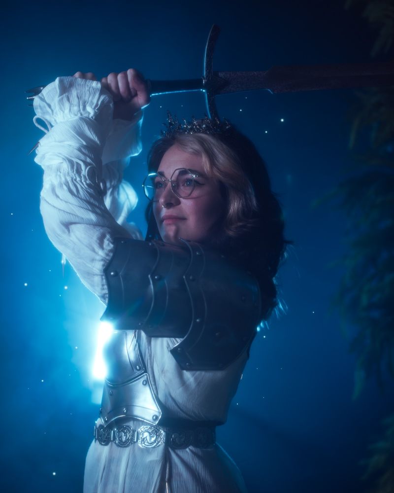 Close up of girl in a white dress and armor holding up a sword
