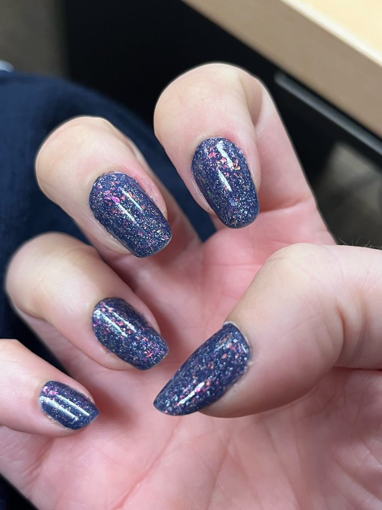 A close up of the same woman's other hand. Now cold, the thermal nail polish is entirely dark grey-blue with vivid pink flakes