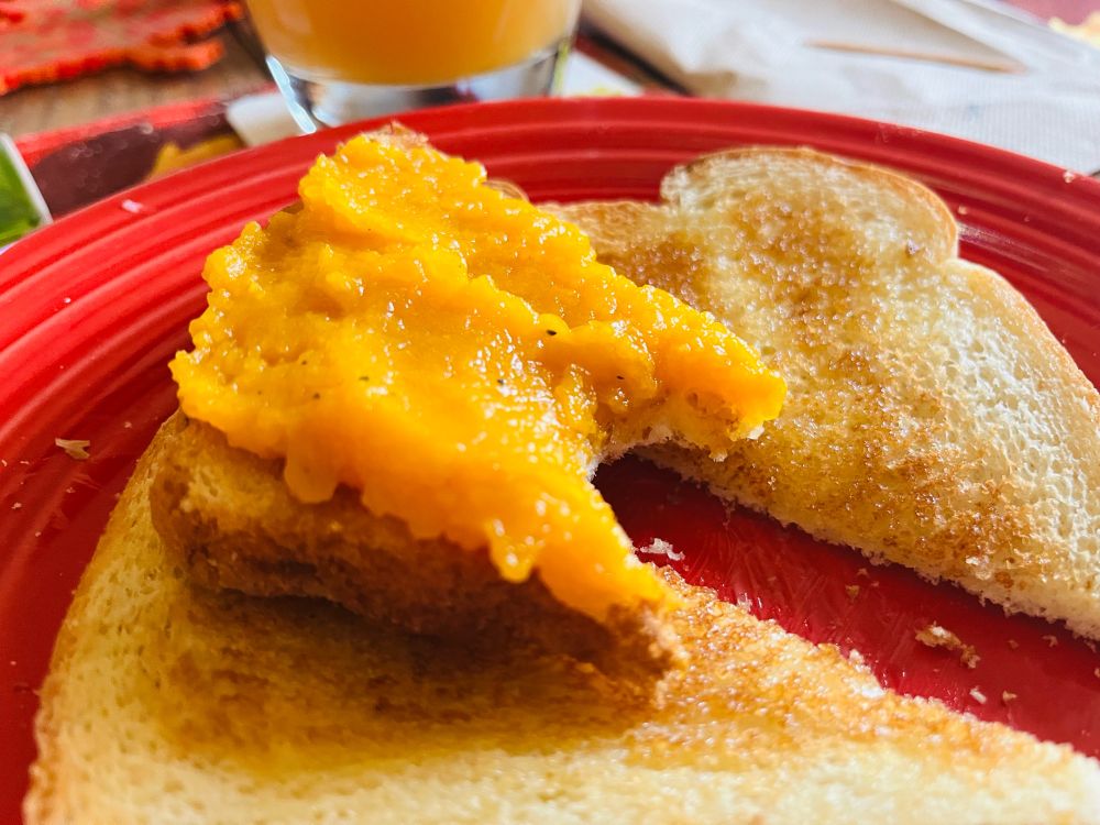 A piece of white bread toast, diagonally sliced, with mashed butternut squash on top. The slice of toast is sitting on top of two other slices of buttered toast.