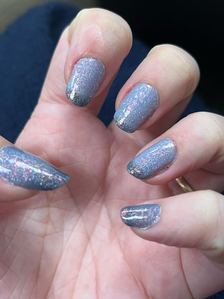 A close up of a woman's hand. The nails are painted with a thermal polish that is part pale grey-blue and part dark grey-blue with vivid pink flakes