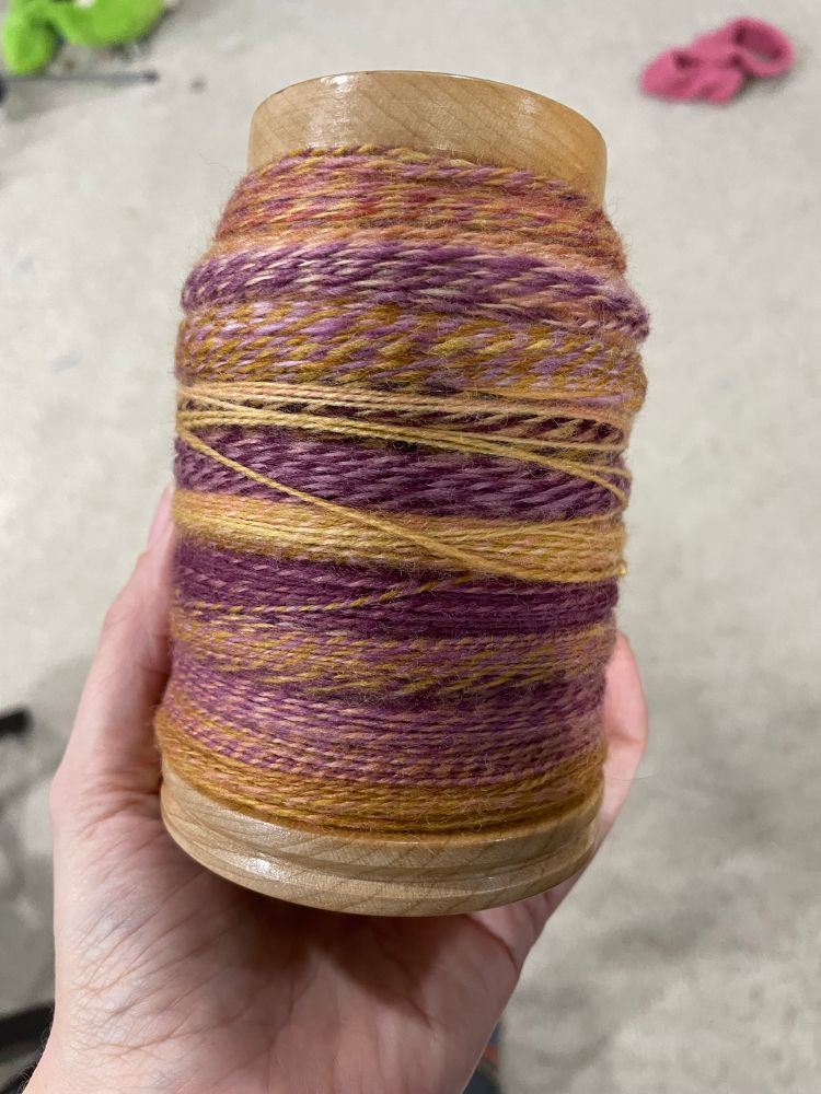 A VERY full bobbin of pink, orange, and purple yarn