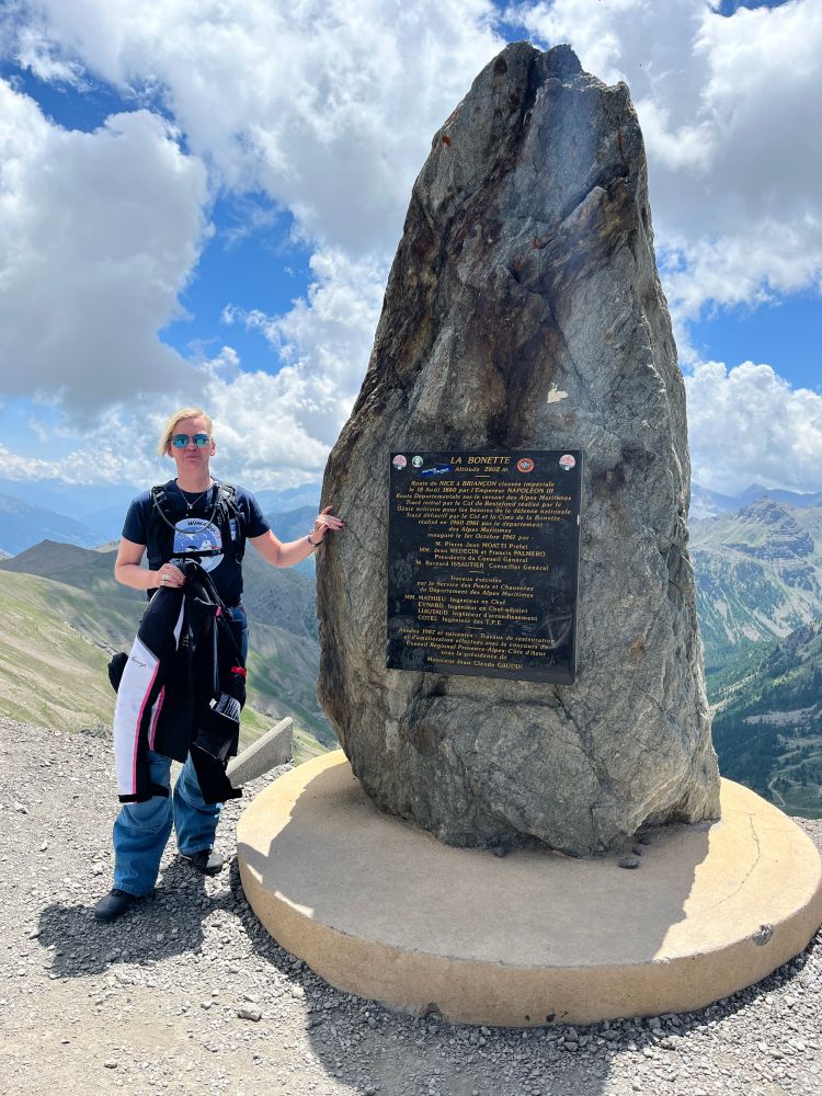 Picture of a biker standing by a marker stone at "La Bonette" in French Alps. Alps in the background