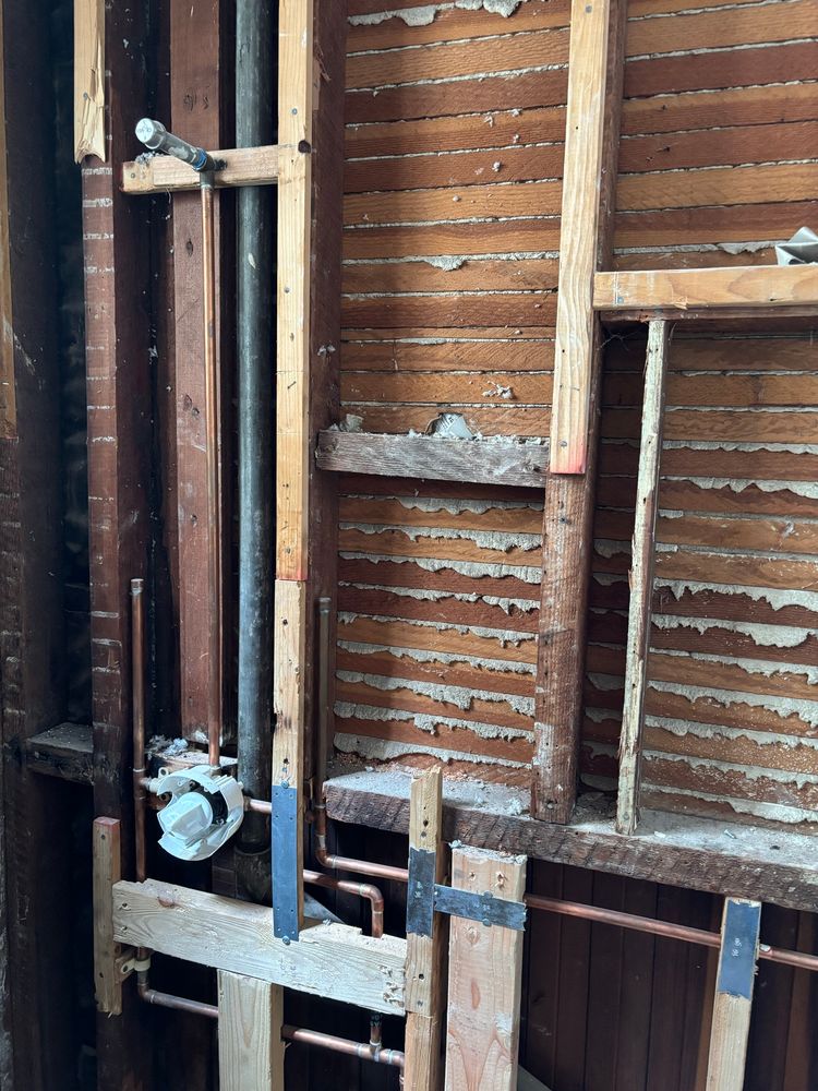 A gutted bathroom wall revealing some beams and 119 year old plaster between wood strips