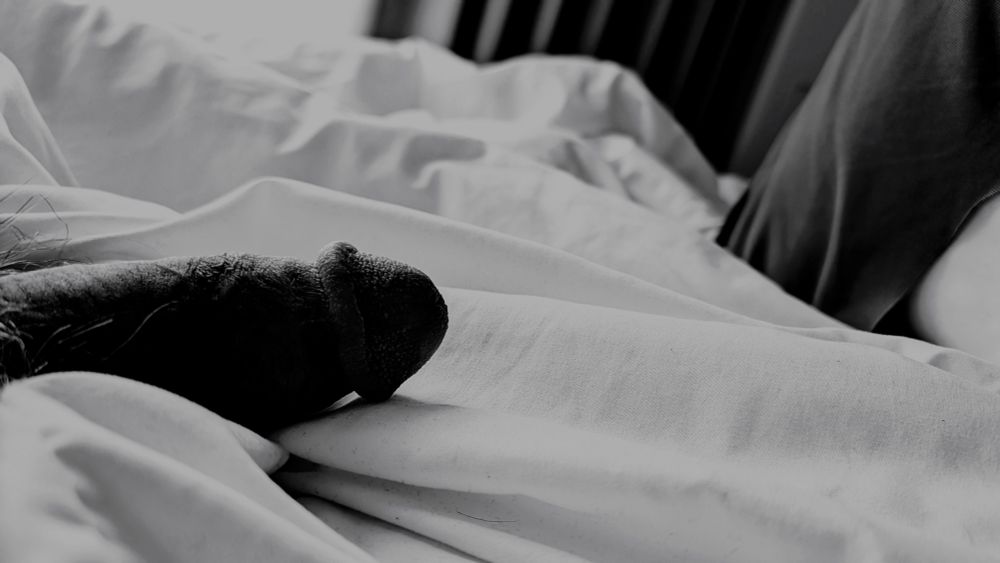 A black and white photo of a half-erect penis flopped over some white sheets
