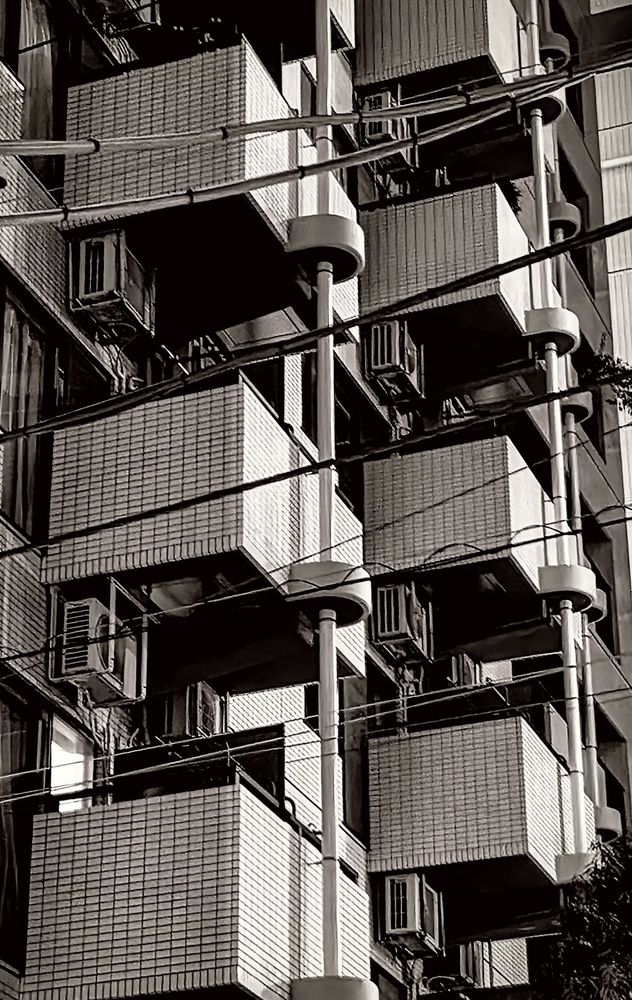 A close-up of a geometrically interesting series of balconies seen on a highrise apartment building. Power lines cross in front of the frame. The balconies appear staggered.