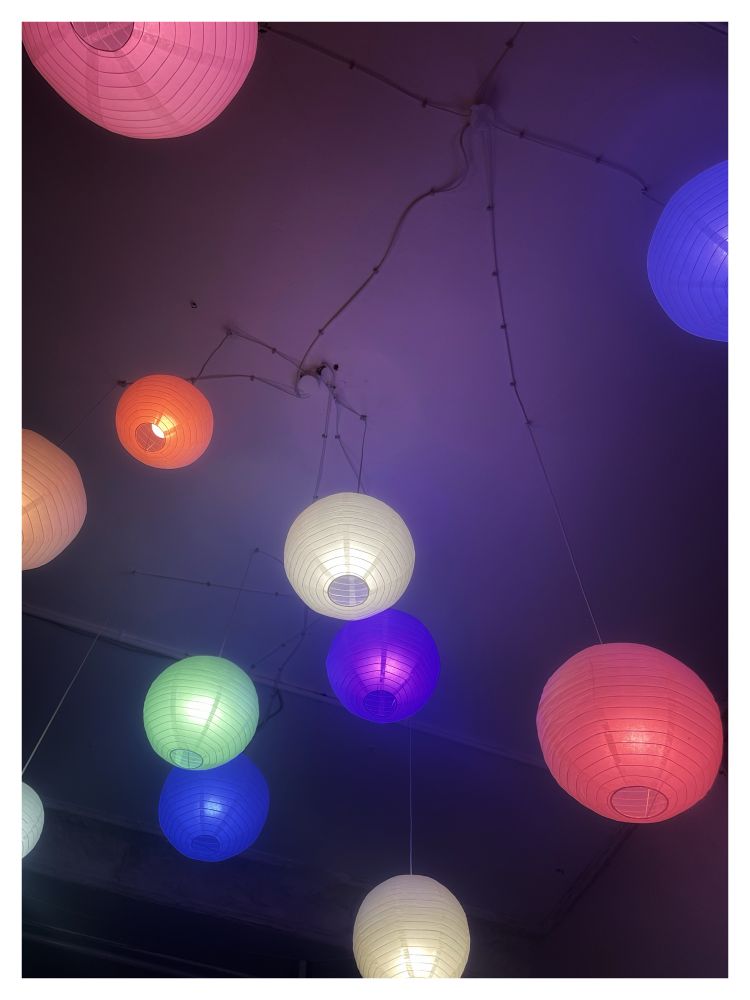 Lampenschirme mit bunten Birnen strahlen von einer weißen Decke.