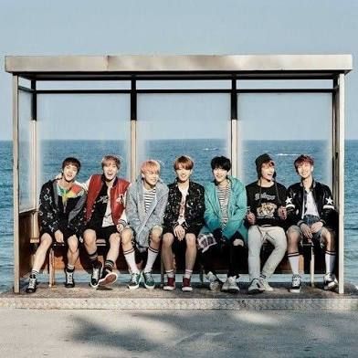 BTS sitting on the famous Speing Day bench with the ocean behind them.