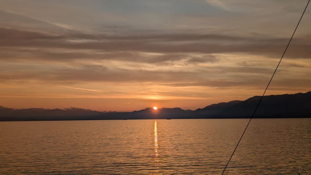 Sun just rising over Naples and Mount Vesuvius. Picture taken from the vantage point of a yacht out at sea with calm waters. The sun lays down a line of golden reflection heading towards the viewer.