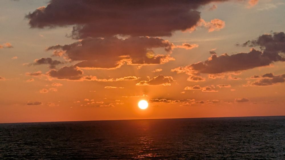 Sunrise over the open ocean with the sun just fully above the horizon. The sky is filled with pinks and oranges with some scattered cloud. 