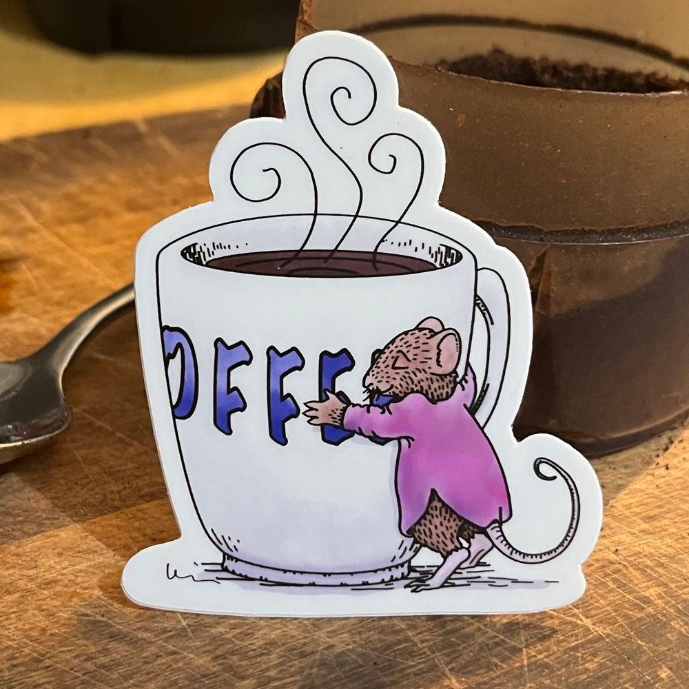 A sticker of a white coffee cup being hugged by a brown mouse in a pink dress/tunic. Part of the word coffee is . The illustration was done digitally with black lines and color fills. The stick propped up against the top of Filled with ground coffee. It is about 3 inches tall.