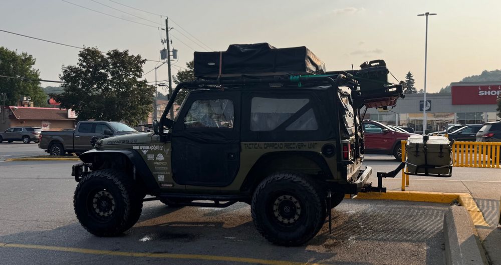 A jeep with items on the hood, roof, and on two platforms stuck to the back. 