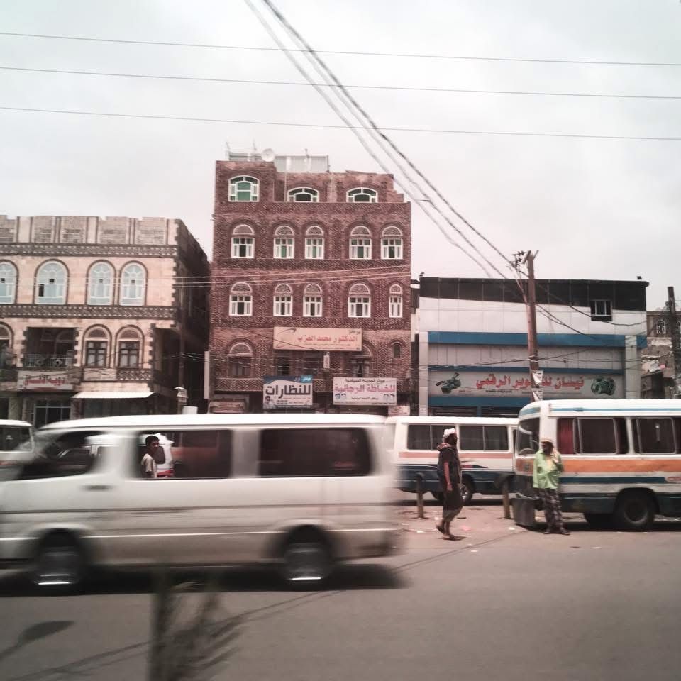Men walk between minibuses on a street of shops.  