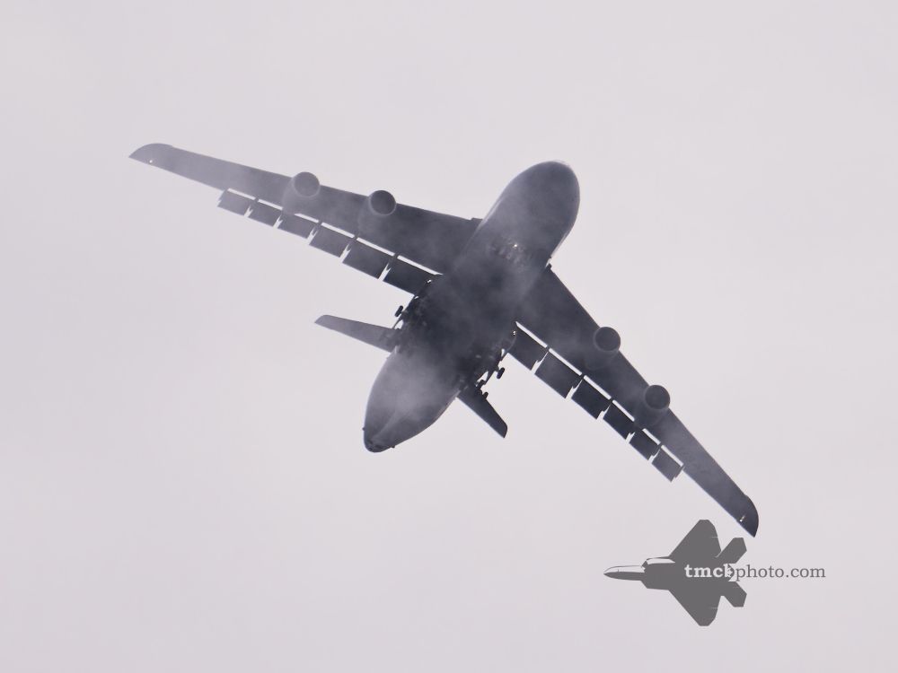 A C-5M with gear down emerges from the cloud layer.