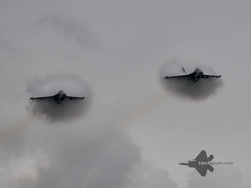 Two US Navy EA-18G Growlers from the US Navy Growler Airshow Team fly in a formation high speed pass, creating two vapour cones on an overcast day. 