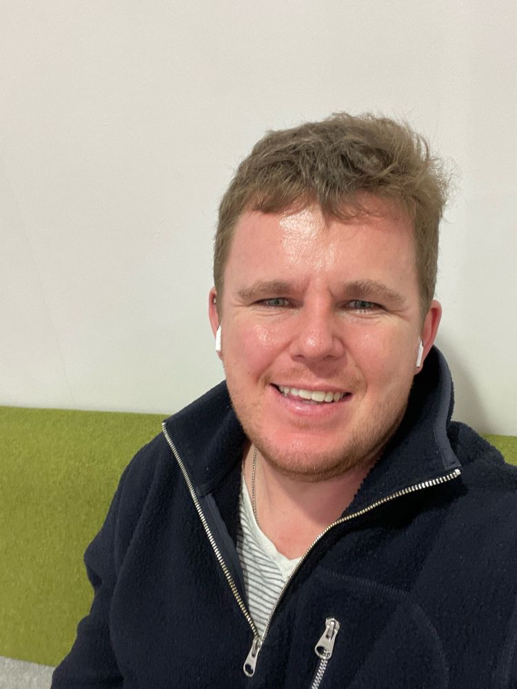 Me sat on a green chair waiting for laundry in a blue fleece and white T-shirt