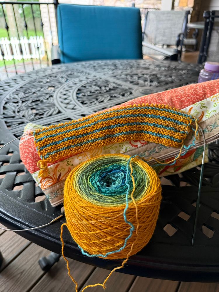 Yellow and teal garter stitch knitting on a black wrought iron table. 