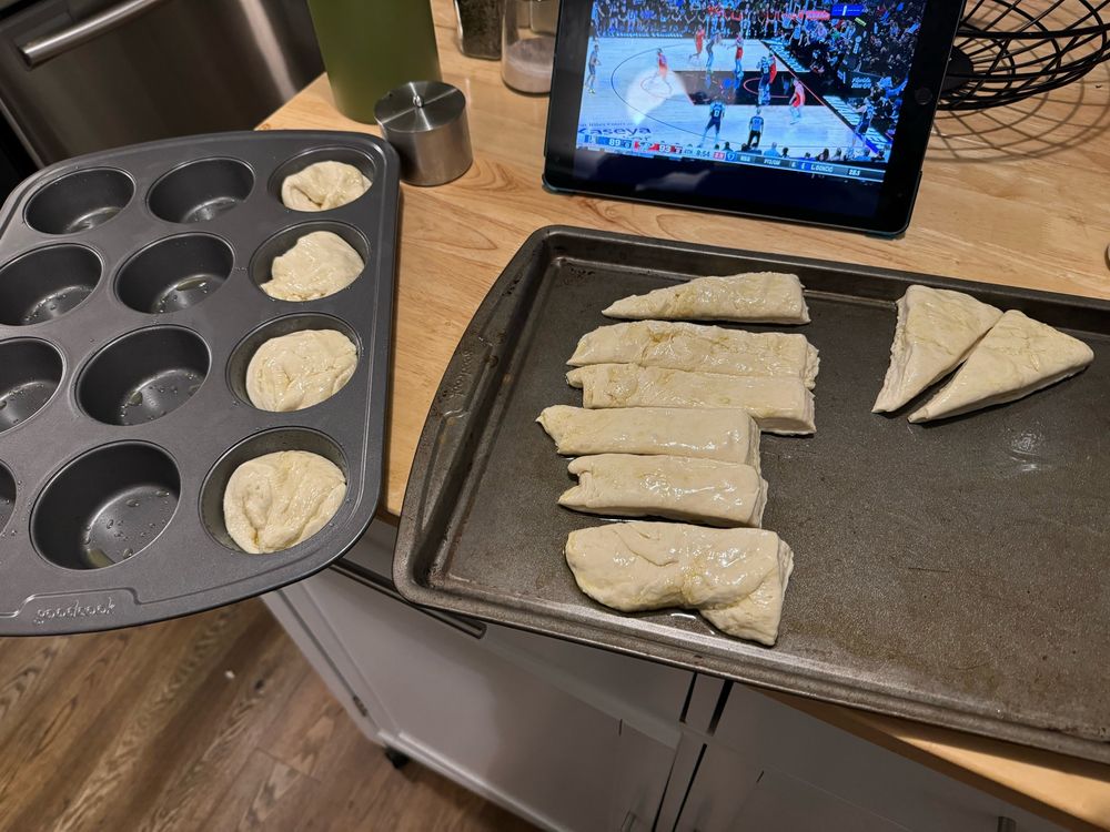 Pieces of dough sit on a baking sheet while others are seen in a muffin tin